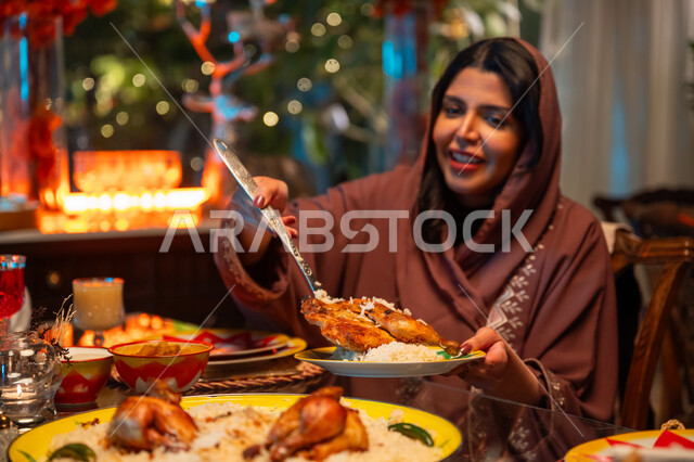 مائدة مليئة بالأطعمة والمشروبات الشهية, تناول الافطار الرمضاني عند أذان المغرب, تعابير السعادة والسرور بلمة الأهل، امرأة عربية خليجية سعودية تقوم بسكب صحن من الأرز مع الدجاج المشوي، جلسة عائلية رمضانية روحانية، زينة وديكور شهر رمضان المبارك