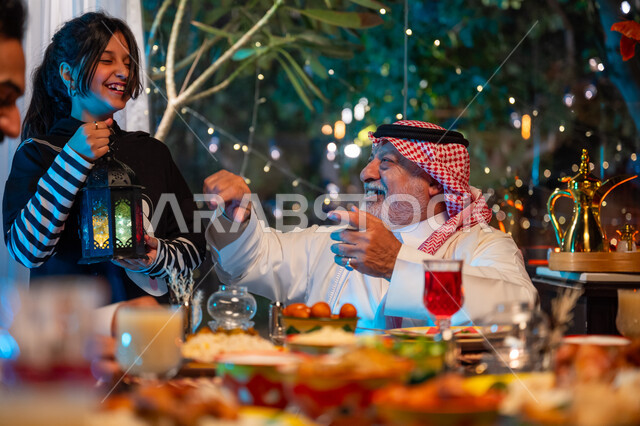 ديكور وزينة شهر رمضان المبارك، تعابير السعادة والسرور بلمة الأهل، مائدة مليئة بالأطعمة والمشروبات الشهية, الاستمتاع بقضاء الوقت مع الأسرة، جلسة عائلية رمضانية روحانية، عائلة عربية خليجية سعودية تجلس على طاولة الطعام لتناول الافطار الرمضاني عند أذان المغرب