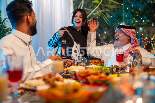 ايماءات السعادة والسرور بلمة الأهل، مائدة مليئة بالأطعمة والمشروبات الشهية, الاستمتاع بقضاء الوقت مع الأسرة، جلسة عائلية رمضانية روحانية، ديكور وزينة شهر رمضان المبارك، عائلة عربية خليجية سعودية تجلس على طاولة الطعام لتناول الافطار الرمضاني عند أذان المغرب