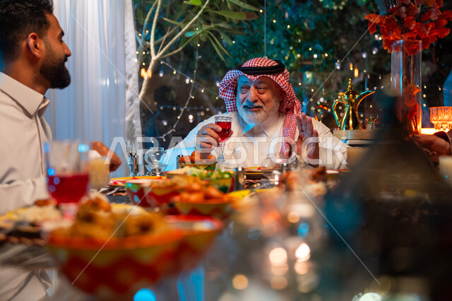 ديكور وزينة شهر رمضان المبارك، جلسة عائلية رمضانية روحانية، قضاء وقت ممتع مع الأسرة، مائدة مليئة بالأطعمة والمشروبات الشهية, ايماءات السعادة والسرور بلمة الأهل، عائلة عربية خليجية سعودية تجلس على طاولة الطعام لتناول الافطار الرمضاني عند أذان المغرب