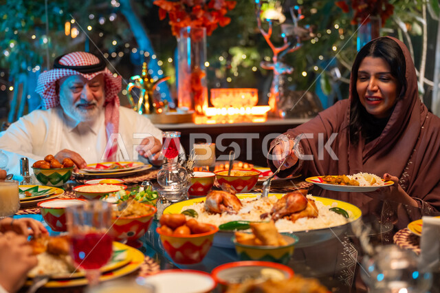 زينة وديكور شهر رمضان المبارك، ايماءات السعادة والسرور بلمة الأهل، مائدة مليئة بالأطعمة والمشروبات الشهية, قضاء وقت ممتع مع الأسرة، جلسة عائلية رمضانية روحانية، عائلة عربية خليجية سعودية تجلس على طاولة الطعام لتناول الافطار الرمضاني عند أذان المغرب