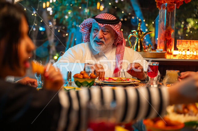 تعابير السعادة والسرور بلمة الأهل، مائدة مليئة بالأطعمة والمشروبات الشهية, قضاء وقت ممتع مع الأسرة، جلسة عائلية رمضانية روحانية، زينة وديكور شهر رمضان المبارك، عائلة عربية خليجية سعودية تجلس على طاولة الطعام لتناول الافطار الرمضاني عند أذان المغرب