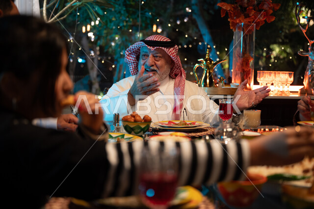 مائدة مليئة بالأطعمة والمشروبات الشهية, قضاء وقت ممتع مع الأسرة، جلسة عائلية رمضانية روحانية، زينة وديكور شهر رمضان المبارك، تعابير السعادة والسرور بلمة الأهل، عائلة عربية خليجية سعودية تجلس على طاولة الطعام لتناول الافطار الرمضاني عند أذان المغرب