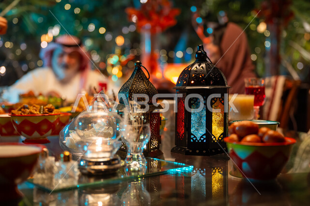 Happy Ramadan religious family atmosphere, exchanging conversations between family members, colorful decorated metal lanterns on a table filled with delicious oriental foods, a Saudi Arabian Gulf family gathered around the dining table, performing the fasting duty in the holy month of Ramadan, Islamic occasion decorations