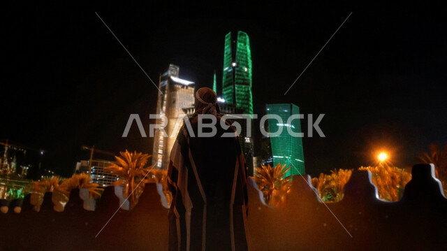 اليوم الوطني السعودي 23 سبتمبر, صورة من الخلف لرجل عربي خليجي سعودي يرتدي زي المناسبة الوطنية ينظر إلى الأبراج المضيئة باللون الاخضر في الليل، ذكرى تأسيس الدولة السعودية الأولى 22 فبراير, يوم بدينا 1727م, النمو والتطور العمراني