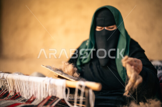 حرفة يدوية تاريخيه, يوم بدينا 22 فبراير، الشغف في ممارسة مهنة الغزل و النسج, المحافظة على التراث الشعبي السعودي, ذكرى تأسيس الدولة السعودية الأولى 1727م, صورة مقربة لامرأة عربيه خليجية سعودية ترتدي البرقع و العباءه السوداء تجلس في بيت من الطين تقوم بلف خيوط الصوف