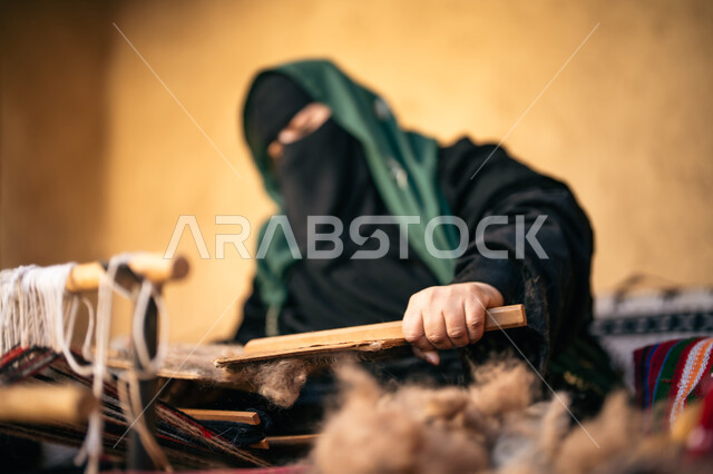 حرفة يدوية تاريخيه, يوم بدينا 22 فبراير، الشغف في ممارسة مهنة الغزل و النسج, المحافظة على التراث الشعبي السعودي, ذكرى تأسيس الدولة السعودية الأولى 1727م, صورة مقربة لامرأة عربيه خليجية سعودية ترتدي البرقع و العباءه السوداء تجلس في بيت من الطين تقوم بلف خيوط الصوف