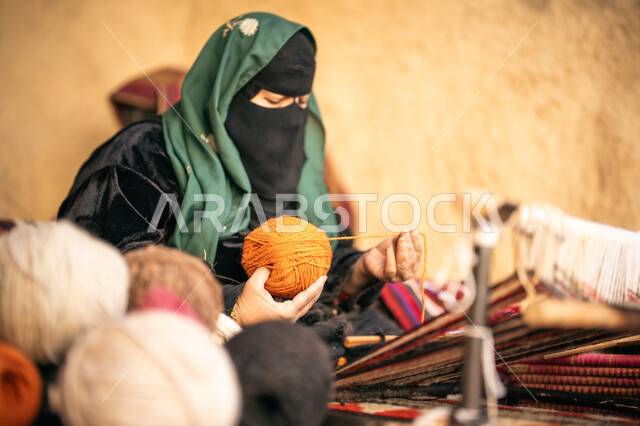 حرفة يدوية تاريخيه, يوم بدينا 22 فبراير، الشغف في ممارسة مهنة الغزل و النسج, المحافظة على التراث الشعبي السعودي, ذكرى تأسيس الدولة السعودية الأولى 1727م,  امرأة عربيه خليجية سعودية ترتدي البرقع و العباءه السوداء تجلس في بيت من الطين تقوم بلف خيوط الصوف