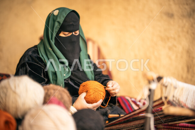 Our day is February 22, the anniversary of the founding of the first Saudi state in 1727 AD, a historical handicraft, the passion for practicing the profession of spinning and weaving, preserving Saudi folk heritage, a picture from the side of a Saudi Gulf Arab woman wearing a burqa and black abaya, winding wool threads