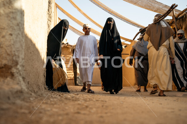 مجموعة من الأشخاص في سوق شعبي، يوم بدينا22 فبراير، ذكرى تأسيس الدولة السعودية الأولى1727 م، تجميع الحطب بموسم الشتاء, صورة من الخلف لرجل عربي خليجي سعودي يرتدي الثوب التقليدي والغترة يحمل الخشب الثقيل ويمشي في حي تاريخي