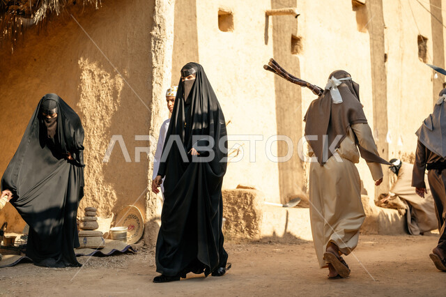 مجموعة من الأشخاص في سوق شعبي، يوم بدينا22 فبراير، ذكرى تأسيس الدولة السعودية الأولى1727 م، تجميع الحطب بموسم الشتاء, صورة من الخلف لرجل عربي خليجي سعودي يرتدي الثوب التقليدي والغترة يحمل الخشب الثقيل ويمشي في حي تاريخي