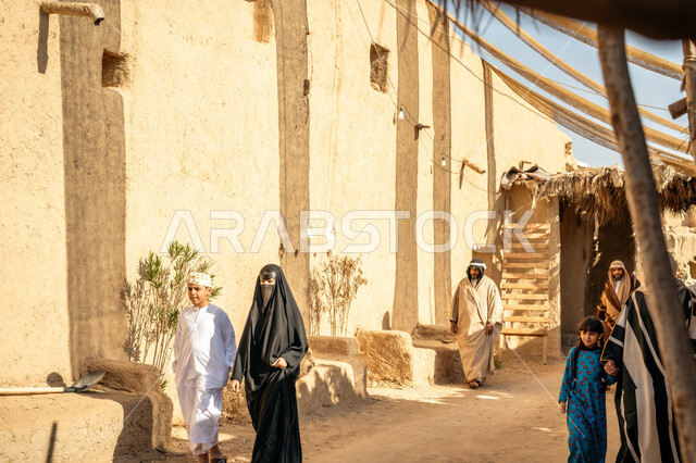 مجموعة من الأشخاص في سوق شعبي، يوم بدينا22 فبراير، ذكرى تأسيس الدولة السعودية الأولى1727 م، تجميع الحطب بموسم الشتاء, صورة مقربة من الخلف لرجل عربي خليجي سعودي يرتدي الثوب التقليدي والغترة يحمل الخشب الثقيل ويمشي في حي تاريخي، قماش ممتد بين البيوت لتوفير الظل