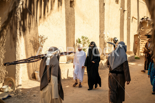 مجموعة من الأشخاص في سوق شعبي، يوم بدينا22 فبراير، ذكرى تأسيس الدولة السعودية الأولى1727 م، تجميع الحطب بموسم الشتاء, صورة من الخلف لرجل عربي خليجي سعودي يرتدي الثوب التقليدي والغترة يحمل الخشب الثقيل ويمشي في حي تاريخي