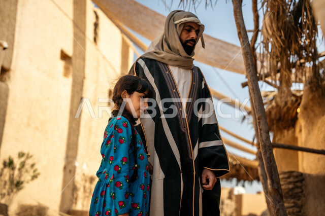 مظلة قماشية ممتدة بين البيوت، توفير الظل بطريقة قديمة متوارثة،  يوم بدينا22 فبراير، ذكرى تأسيس الدولة السعودية الأولى1727 م، رجل عربي خليجي سعودي يرتدي البشت والغترة  يتجول مع ابنته  في الحي التاريخي المبني على الطراز القديم