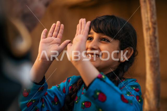 قضاء وقت ممتع مع الأب، ألعاب متوارثة من الأجداد عبر الأجيال، بنت عربية خيليجية سعودية ترتدي فستان أزرق تقوم باللعب والمرح برفقة والدها بإيماءات السعادة والسرور، إحياء ذكرى تأسيس الدولة السعودية الأولى 1727 م, يوم بدينا 22 فبراير, منزل طيني قديم في قرية تاريخية