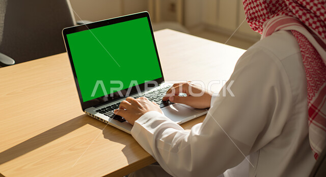 Browsing the internet using a laptop, integrating modern technology into work life, using a laptop to manage business and hold remote meetings, close-up side view of a Saudi Arabian Gulf man wearing a traditional thobe and shemagh sitting at a desk, typing on a keyboard, chroma key