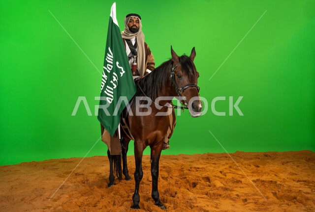 يوم بدينا 22 فبراير، ذكرى تأسيس الدولة السعودية الأولى1727م, الفخر والاعتزاز بالهوية الوطنية، شغف تربية ورعاية الخيل، اليوم الوطني السعودي 23 سبتمبر، بورتريه لرجل عربي خليجي سعودي يرتدي الزي الشعبي يمتطي فرس عربي يحمل علم التأسيس فوق الرمال الناعمة، خلفية خضراء، كروما