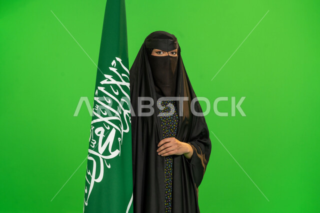 ذكرى تأسيس الدولة السعودية الأولى1727م, اليوم الوطني السعودي 23 سبتمبر، بورتريه لامرأة عربية خليجية سعودية ترتدي البرقع والعباءة تمسك علم المملكة تنظر إلى الكاميرا، يوم بدينا 22 فبراير, يوم العلم 11 مارس، حب الوطن والانتماء إليه، خلفية خضراء، كروما