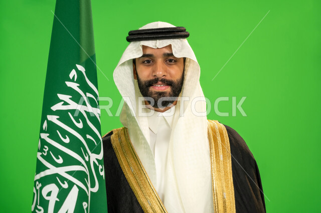 ارتداء الزي الشعبي في مناسبة وطنية, ذكرى تأسيس الدولة السعودية الأولى1727م, اليوم الوطني السعودي 23 سبتمبر، يوم العلم 11 مارس، يوم بدينا22 فبراير, الفخر بالانتماء للوطن, بورتريه مقرب لرجل عربي خليجي سعودي يرتدي البشت والغترة يمسك علم المملكة، خلفية خضراء، كروما