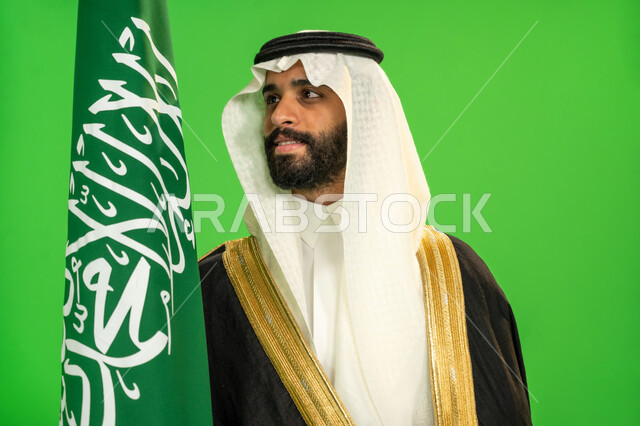 ذكرى تأسيس الدولة السعودية الأولى1727م, اليوم الوطني السعودي 23 سبتمبر، يوم العلم 11 مارس، ارتداء الزي الشعبي في مناسبة وطنية, يوم بدينا22 فبراير, الفخر بالانتماء للوطن, بورتريه مقرب لرجل عربي خليجي سعودي يرتدي البشت والغترة يمسك علم المملكة، خلفية خضراء، كروما