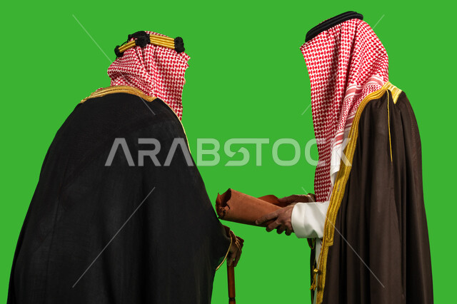 العراقة والاصالة عند العرب، احياء تراث المملكة, يوم بدينا 22 فبراير, ذكرى تأسيس الدولة السعودية الأولى 1727م، ارتداء الزي التقليدي في مناسبة وطنية، بورتريه مقرب من الخلف لرجلين عربيين خليجيين سعوديين يرتديان البشت والشماغ يقومان بقراءة مخطوطة جلد تاريخية، خلفية خضراء، كروما