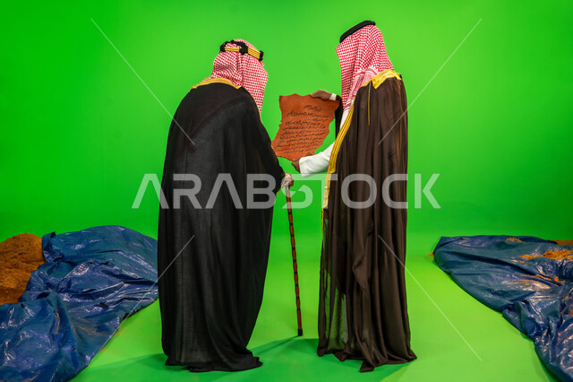 ذكرى تأسيس الدولة السعودية الأولى 1727م، ارتداء الزي التقليدي في مناسبة وطنية, يوم بدينا 22 فبراير, العراقة والاصالة عند العرب، بورتريه من الخلف لرجلين عربيين خليجيين سعوديين يرتديان البشت والشماغ يقومان بقراءة مخطوطة جلد تاريخية، الطول الكامل للجسم، خلفية خضراء، كروما