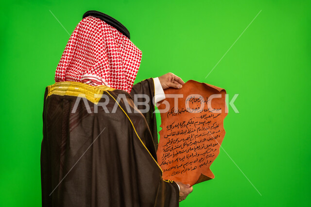 الاصالة والعراقة عند العرب، ذكرى تأسيس الدولة السعودية الأولى 1727م، ارتداء الزي التقليدي في مناسبة وطنية, يوم بدينا 22 فبراير, بورتريه مقرب من الخلف لرجل عربي خليجي سعودي يرتدي البشت والشماغ يقوم بقراءة مخطوطة جلد تاريخية، خلفية خضراء، كروما