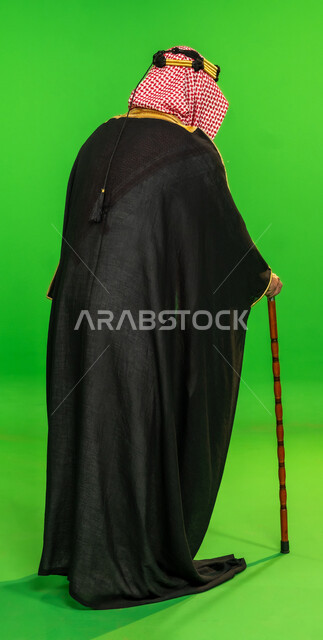 ذكرى تأسيس الدولة السعودية الأولى 1727م، العراقة والاصالة عند العرب، ارتداء الزي التقليدي في مناسبة وطنية، يوم بدينا 22 فبراير, بورتريه من الخلف لرجل عربي خليجي سعودي يرتدي البشت والشماغ يمسك بيده عصا للاتكاء، الطول الكامل للجسم، خلفية خضراء، كروما