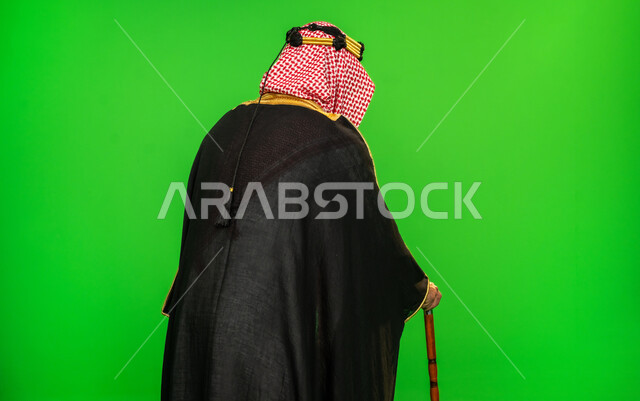 مفهوم العراقة والاصالة عند العرب، ارتداء الزي التقليدي في مناسبة وطنية، ذكرى تأسيس الدولة السعودية الأولى 1727م، يوم بدينا 22 فبراير, بورتريه مقرب من الخلف لرجل عربي خليجي سعودي يرتدي البشت والشماغ يمسك بيده عصا للاتكاء، خلفية خضراء، كروما