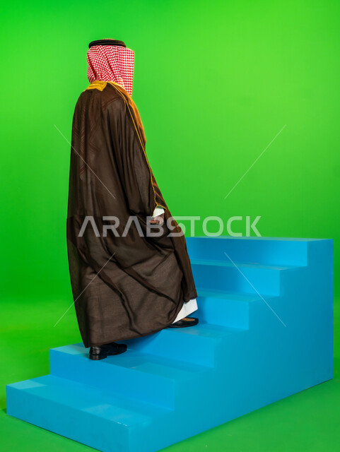The day we started, February 22, authenticity and antiquity among Arabs, wearing traditional dress on a national occasion, the anniversary of the founding of the first Saudi state 1727 AD, a side portrait of a Saudi Gulf Arab man wearing a bisht and a shemagh climbing a blue staircase, full body length, green background, chroma key