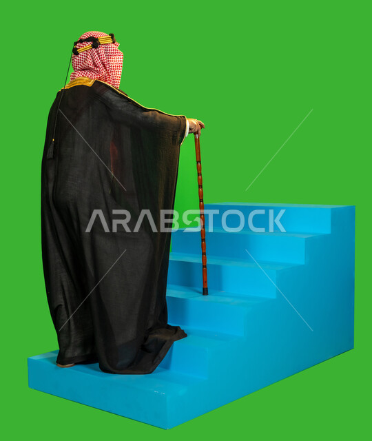 العراقة والاصالة عند العرب، ذكرى تأسيس الدولة السعودية الأولى 1727م، ارتداء الزي التقليدي في مناسبة وطنية، يوم بدينا 22 فبراير, بورتريه من الجانب لرجل عربي خليجي سعودي يرتدي البشت والغترة يمسك بيده عصا للاتكاء يصعد على درج أزرق، الطول الكامل للجسم، خلفية خضراء، كروما
