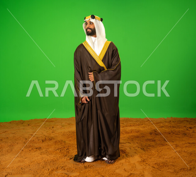 الاعتزاز والفخر بالهوية الوطنية، يوم بدينا22 فبراير، ذكرى تأسيس الدولة السعودية الأولى1727م, ارتداء الزي الشعبي في مناسبة وطنية, بورتريه لرجل عربي خليجي سعودي يرتدي البشت والعقال يقف باستقامة على الرمال الناعمة، الطول الكامل للجسم، خلفية خضراء، كروما