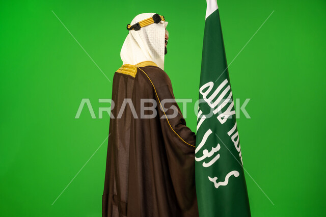 ذكرى تأسيس الدولة السعودية الأولى1727م, حب الوطن والانتماء اليه، يوم بدينا22 فبراير, الاعتزاز والفخر بالهوية الوطنية، ارتداء الزي الشعبي في مناسبة وطنية, بورتريه من الجانب لرجل عربي خليجي سعودي يرتدي البشت والعقال يمسك علم يوم التأسيس، خلفية خضراء، كروما