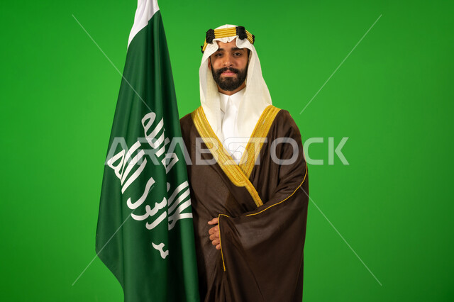 يوم بدينا22 فبراير, الاعتزاز والفخر بالهوية الوطنية، ارتداء الزي الشعبي في مناسبة وطنية, حب الوطن والانتماء اليه، ذكرى تأسيس الدولة السعودية الأولى1727م, بورتريه لرجل عربي خليجي سعودي يرتدي البشت والعقال يمسك علم يوم التأسيس، خلفية خضراء، كروما