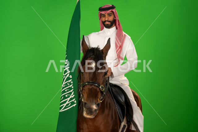 يوم العلم 11 مارس، الاعتزاز والفخر بالهوية الوطنية، شغف تربية ورعاية الخيل، توارث حب الجياد من الاجداد، اليوم الوطني السعودي 23 سبتمبر، بورتريه لرجل عربي خليجي سعودي يرتدي الثوب التقليدي والشماغ يمتطي فرس عربي ويرفع علم السعودية، خلفية خضراء، كروما