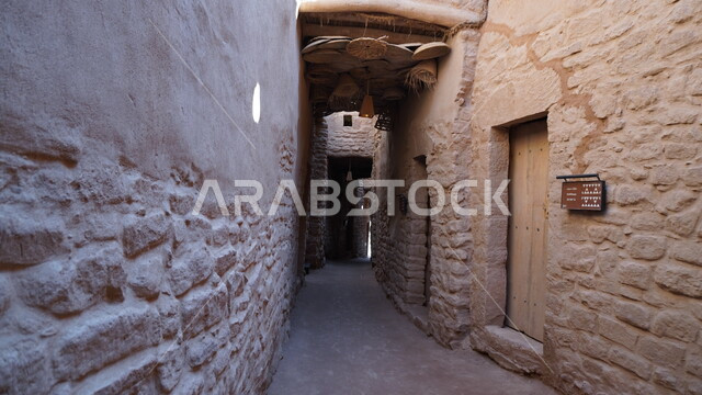 A famous tourist area in the Kingdom of Saudi Arabia, the popular mud houses in the old town, a narrow passageway roofed with palm fronds, tourism in the city of Al-Ula, a historical archaeological building, traditional lamps hanging from the ceiling, ancient mud architectural art