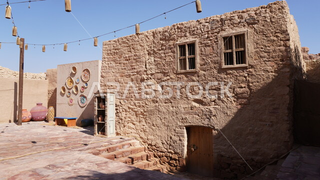 البيوت الطينية الشعبية, مجموعة من المشغولات اليدوية المصنوعة من القش الملونة والمعلقة على جدار في البلدة القديمة, السياحة في مدينة العلا, الاماكن التاريخية التراثية, منطقة سياحية مشهورة في المملكة العربية السعودية، الفن الهندسي المعماري على الطراز الطيني القديم