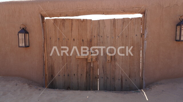 باب بيت طيني شعبي في البلدة القديمة, الفن الهندسي المعماري على الطراز القديم، مبنى تاريخي أثري, منطقة سياحية مشهورة في المملكة العربية السعودية، مكان لجذب واستقطاب السياح من أنحاء العالم، مجموعة من المصابيح المعدنية، السياحة في مدينة العلا