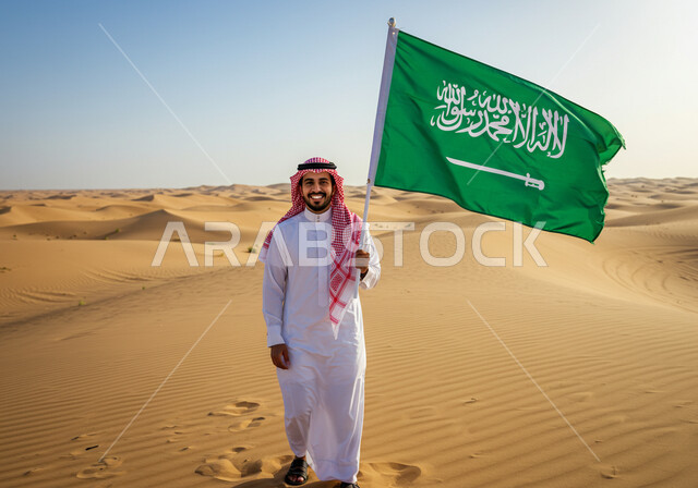Desert and desert environment during the day, Flag Day March 11, a smiling Saudi Arabian Gulf man wearing traditional thobe and shemagh stands on soft sand in the desert holding the Kingdom's flag looking at the camera with proud gestures, Saudi National Day September 23, sand formations in the desert