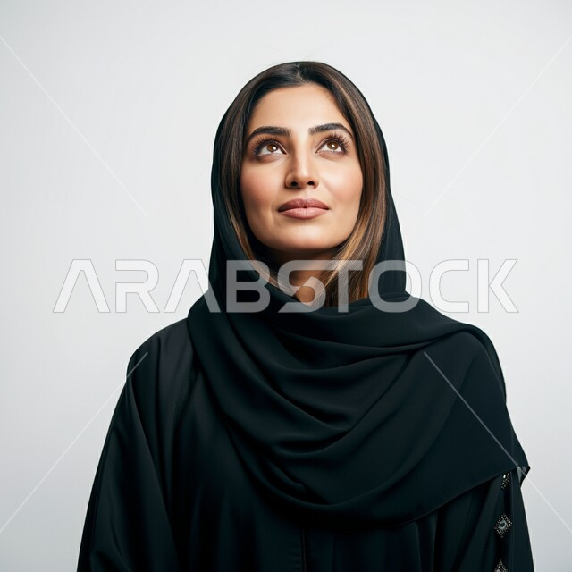 التقاط صور شخصية للوثائق الرسمية، مفهوم الأناقة والأنوثة, بورتريه مقرب لامرأة عربية خليجية سعودية محجبة ترتدي العباءة تنظر إلى شيء ما في الاعلى بايماءات السرور والثقة بالنفس, الاهتمام بالمظهر الخارجي، خلفية بيضاء