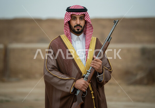 استخدام البندقيه لصيد الحيوانات البرية، توارث مهنة الصيد بين أبناء الوطن، رجل عربي خليجي سعودي يرتدي البشت والشماغ  في المناسبة الوطنية، يوم بدينا ٢٢ فبراير ، ذكرى تاسيس الدوله السعوديه الاولى ١٧٢٧ م، النظر الى الكاميرا بايماءات الفخر،  حمل السلاح للدفاع عن الوطن