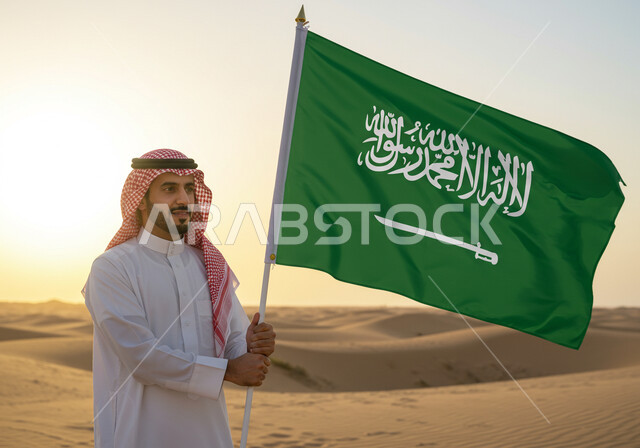 Our day is February 22nd, wearing traditional costume on a national occasion, a Saudi Arabian Gulf man wearing traditional dress and shemagh stands on the golden sands of the desert holding the flag of the Kingdom of Saudi Arabia, Saudi National Day September 23rd, Flag Day March 11th, anniversary of the founding of the first Saudi state 1727 AD