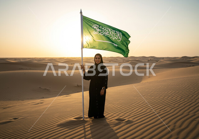 ذكرى تأسيس الدولة السعودية الأولى 1727م,  المحافظة على التراث السعودي، يوم بدينا 22 فبراير, حب الوطن والانتماء إليه، سيدة عربية خليجية سعودية ترتدي الحجاب والعباءة تقف وسط الصحراء وبجانبها علم المملكة