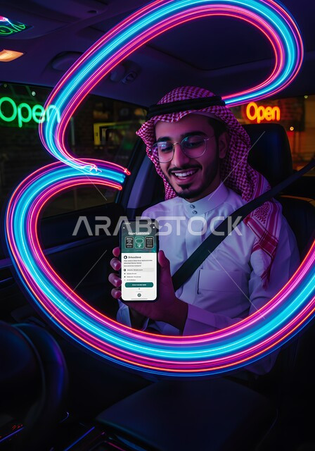 عرض تطبيق وخدمة الهاتف المحمول, استخدام التكنولوجيا الحديثة للتسوق الالكتروني عبر الانترنت, صورة مقربة لشاب عربي خليجي سعودي مبتسم يرتدي الشماغ والثوب التقليدي يجلس في السيارة يحمل بيده الجوال بتعابير السرور، اضواء هولوجرامية ثلاثية الابعاد ملونة