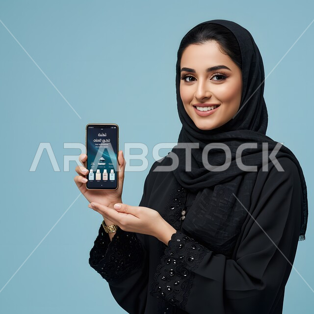 استخدام جهاز تقني حديث، عرض برامج وتطبيقات الجوال، بورتريه مقرب لامرأة عربية خليجية سعودية ترتدي الحجاب والعباءة تمسك بيدها الهاتف المحمول تنظر إلى الكاميرا بإيماءات الثقة بالنفس والسرور، دمج التكنولوجيا المتطورة بالحياة العملية، خلفية زرقاء