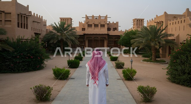 جولة سياحية في المدينة، الأحياء التاريخية الشعبية في المملكة العربية السعودية، صورة من الخلف لرجل عربي خليجي سعودي يرتدي الثوب التقليدي والشماغ ينظر إلى المباني الأثرية أمامه