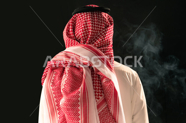 Concept of masculinity and elegance, concern for outward appearance, close-up portrait from behind of a Saudi Arabian Gulf man wearing traditional thobe and shemagh standing straight looking at something, black background