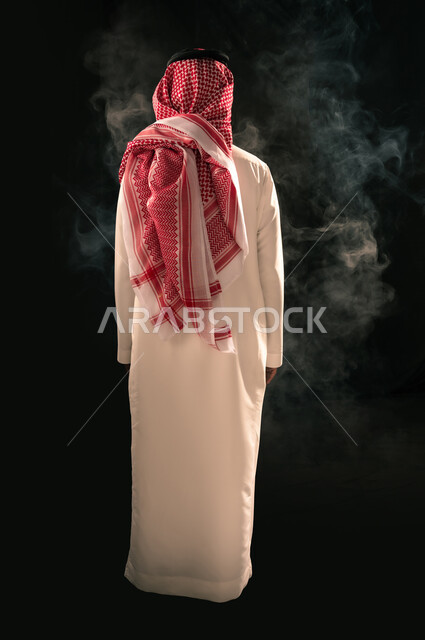 الاهتمام بالمظهر الخارجي، بورتريه من الخلف لرجل عربي خليجي سعودي يرتدي الثوب التقليدي والشماغ يقف باستقامة ينظر إلى شيء ما، مفهوم الرجولة والأناقة، الجسم بالطول الكامل، خلفية سوداء