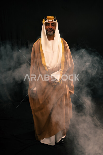 ذكرى تأسيس الدولة السعودية الأولى 1727م، يوم بدينا 22 فبراير، الفخر بإنجازات المملكة، حب الوطن والانتماء إليه, بورتريه لرجل عربي خليجي سعودي يرتدي الغترة والعقال الذهبي والبشت ينظر إلى الكاميرا بإيماءات الشموخ، الجسم بالطول الكامل، خلفية سوداء