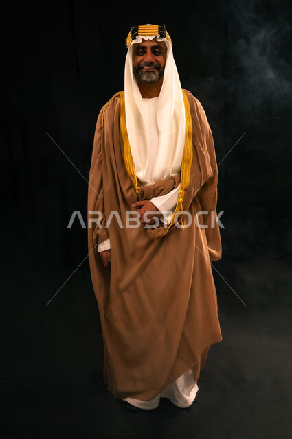 ذكرى تأسيس الدولة السعودية الأولى 1727م، يوم بدينا 22 فبراير، الفخر بإنجازات المملكة، حب الوطن والانتماء إليه, بورتريه لرجل عربي خليجي سعودي يرتدي الغترة والعقال الذهبي والبشت ينظر إلى الكاميرا بإيماءات الشموخ، الجسم بالطول الكامل، خلفية سوداء